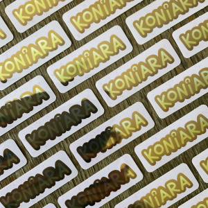 Zdjęcie przestawia ułożone równo złote naklejki z napisem "koniara". Naklejki mają zaokrąglone brzegi, tło jest różowe, a napis złoty.