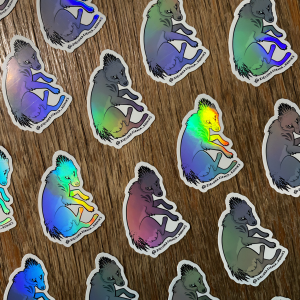 Zdjęcie przestawia naklejki z groźnym stworzeniem znanym jako raya. Raya jest podobna trochę do wilka, a trochę do wilkowora tasmańskiego. Na głowie i zadzie ma kolce. Ma agresywne spojrzenie i zmarszczony w ostrzeżeniu pysk. Naklejki są holograficzne i mienią się tęczowo.