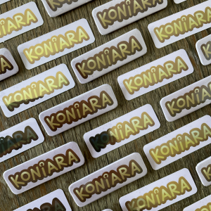 Zdjęcie przedstawia ułożone obok siebie złote naklejki z napisem "koniara" oraz prostokątne przypinki z takim samym napisem.