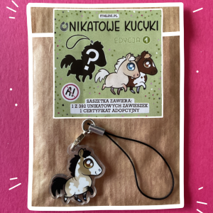Saszetka i leżąca na niej zawieszka ze srokatym konikiem.